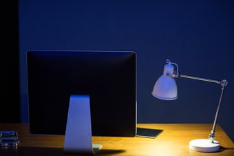 Close-up computer monitor and illuminated lamp on office desk at night